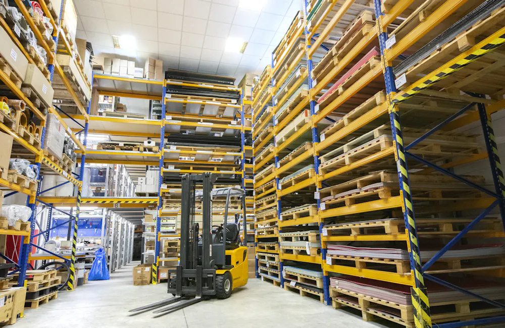 Montacargas moviendo pallets entre estanterías de un almacén