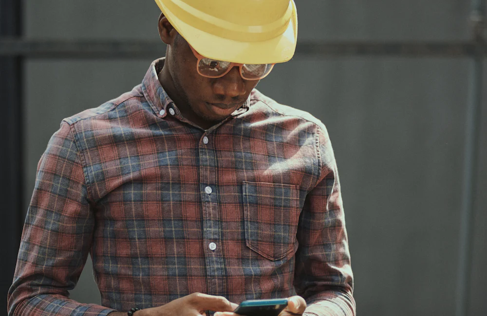 Trabajador con casco de construcción revisando su teléfono celular